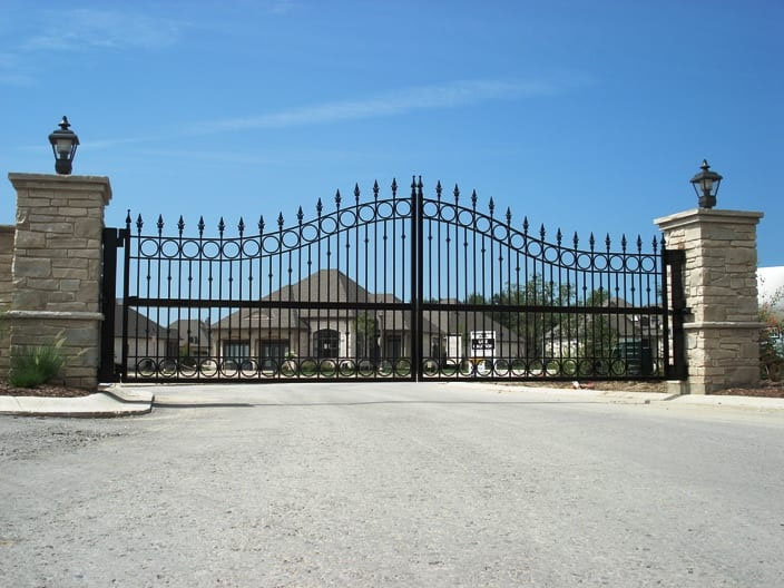 Large custom wrought iron driveway gate with an ornate design, securing a residential property